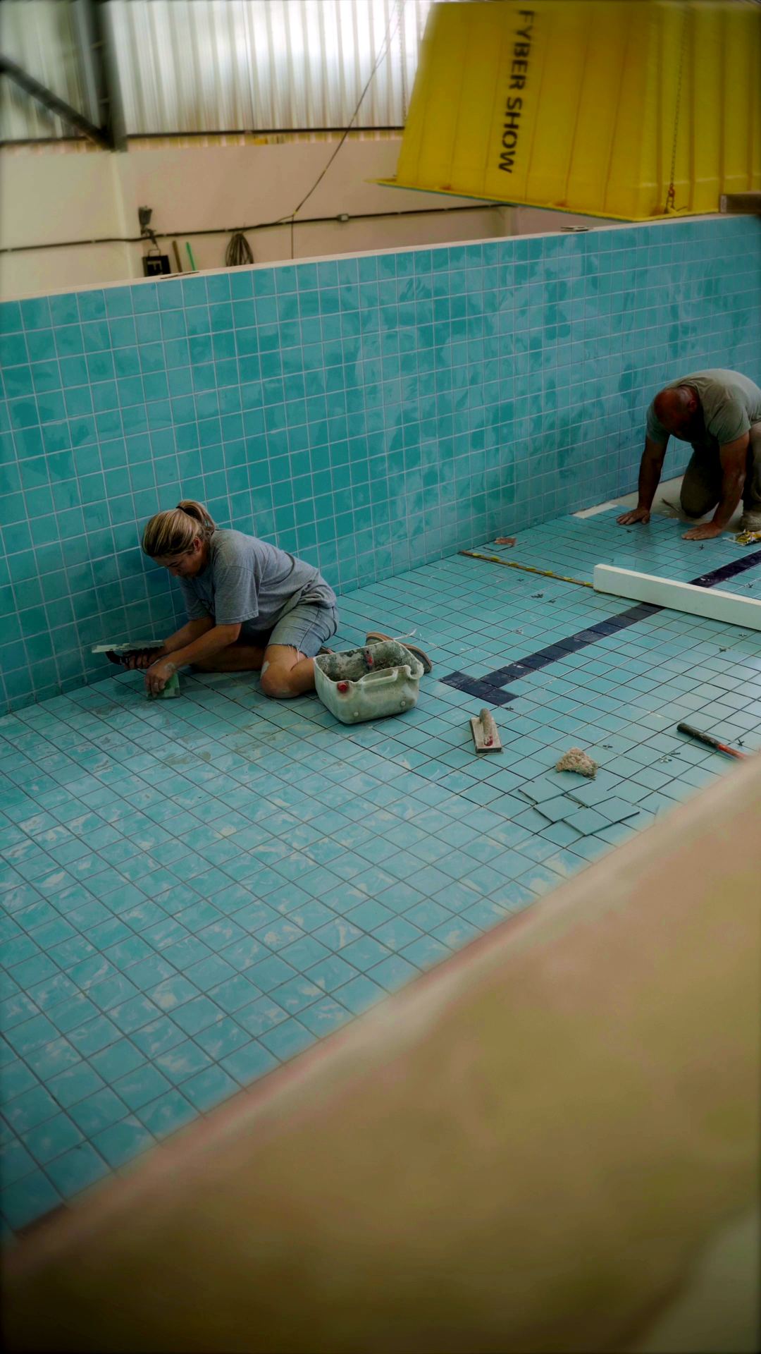 Dois funcionários assentando pastilhas no fundo da piscina, dentro do casco