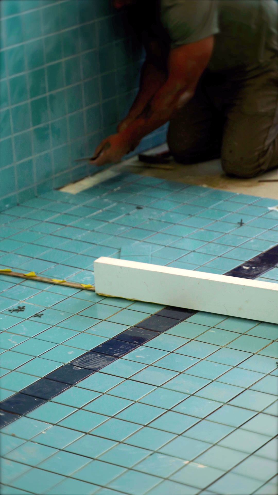 Detalhe das placas de pastilha azul com espaçadores, a faixa azul-escura da raia e uma régua de alinhamento